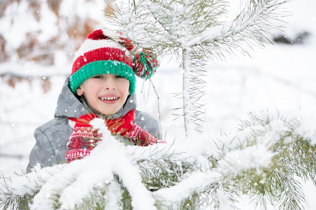 Criança no inverno para passear Garotinho usando um chapéu de Papai Noel em uma floresta de neve