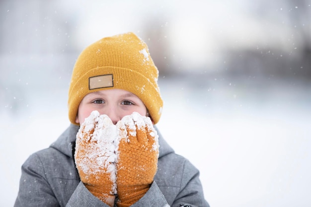 Criança no inverno um garotinho com um chapéu quente e luvas olha para a câmera e sorri