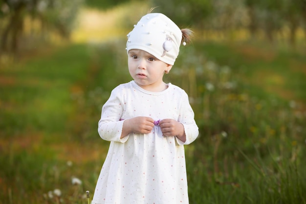 Criança no jardim da primavera Menina engraçada com uma cara triste em um fundo verde