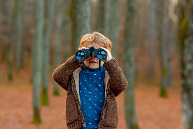 Criança olhando através de binóculos na floresta criança brincando ao ar livre crianças viagens e conceito de aventura