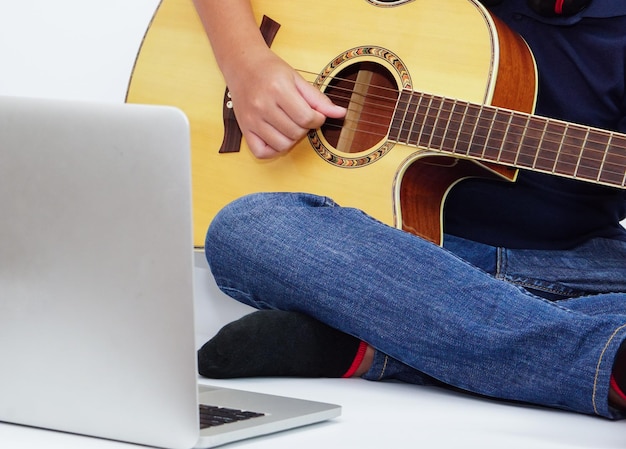 Criança ou adolescente tocando violão usando laptop Aprendendo e relaxando o conceito