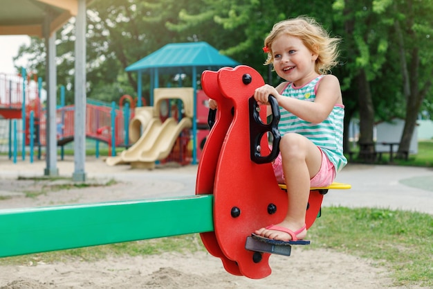 Foto criança pequena brincando no playground no verão sentada em um balanço no parque