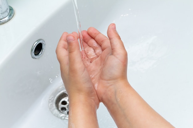 Criança pequena, criança lava as mãos sob a torneira na pia