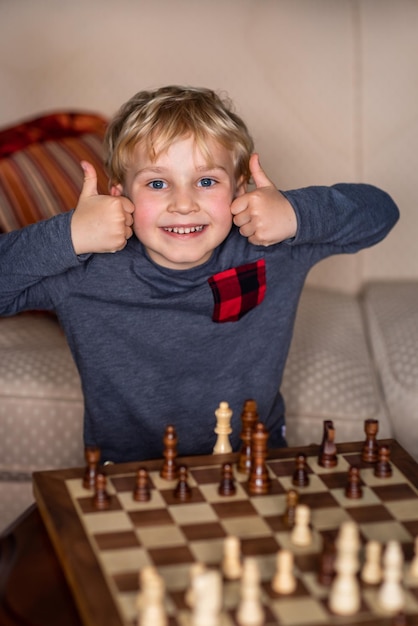 Criança pequena de 5 anos jogando xadrez em um tabuleiro de xadrez grande Tabuleiro de xadrez na mesa em frente ao menino que ele está feliz em ganhar