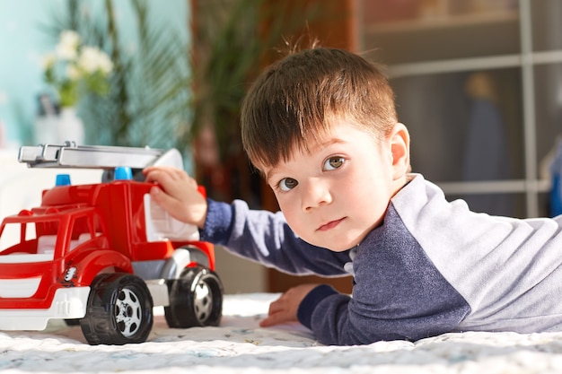 Criança pequena de cabelos escura brinca com carro de brinquedo no quarto