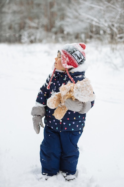 Criança pequena de pé do lado de fora em uma paisagem de inverno segurando um brinquedo macio
