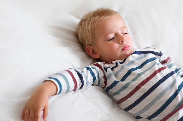 Criança pequena dormindo em cobertor liso branco Pequeno 3 anos de idade Crianças dormem sozinhas em quarto aconchegante Têxtil macio Cabelo loiro sonolento Bebê menino sonhando em uma cama em casa Sinal para banner Espaço para texto