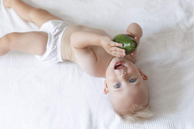 Foto criança pequena e fofa deitada na cama com um abacate nas mãos