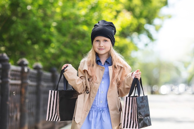 Criança pequena e linda menina fofa e feliz com sacolas de compras nas mãos na rua