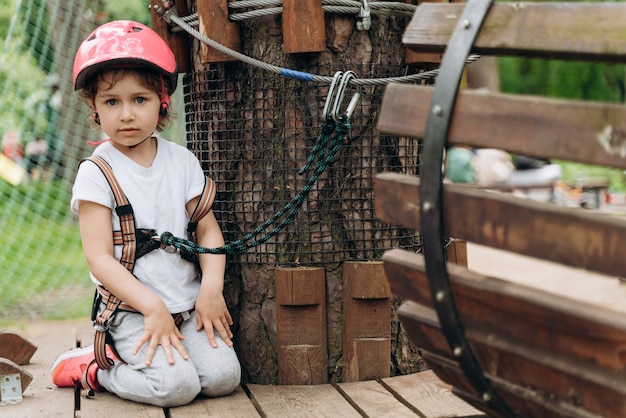 Criança pequena em um parque de cordas passa por obstáculos. Linda, linda garota de seguro e capacete