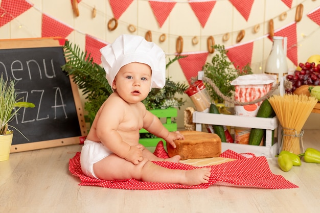 Criança pequena fantasiada de chef sentada entre farinhas e vegetais na cozinha