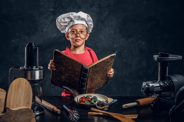 Criança pequena tem uma ótima idéia sobre cozinhar - ele está lendo o livro de receitas.