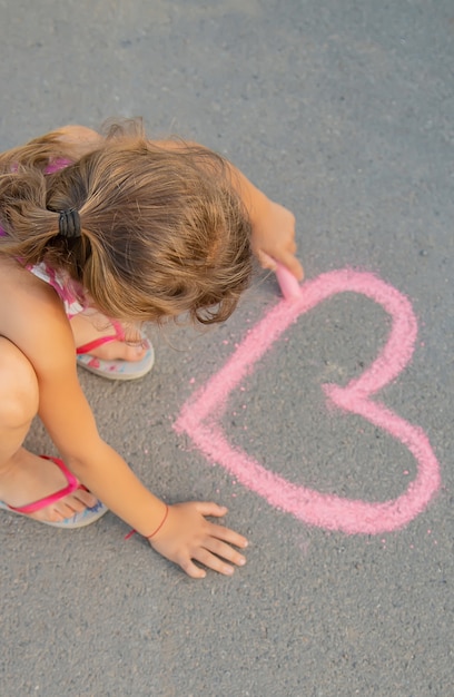 Criança pinta giz no coração de asfalto. foco seletivo.
