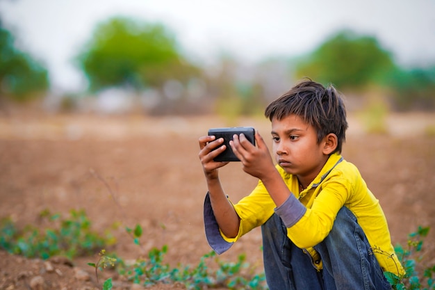 Criança pobre indiana brincando com o celular no campo de agricultura. Cena rural.