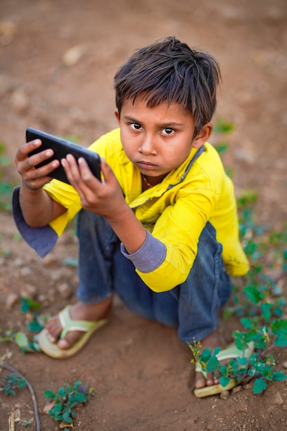 Criança pobre indiana brincando com o celular no campo de agricultura. Cena rural.