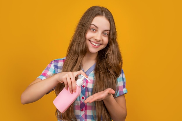 Criança positiva com garrafa de sabonete líquido em fundo amarelo