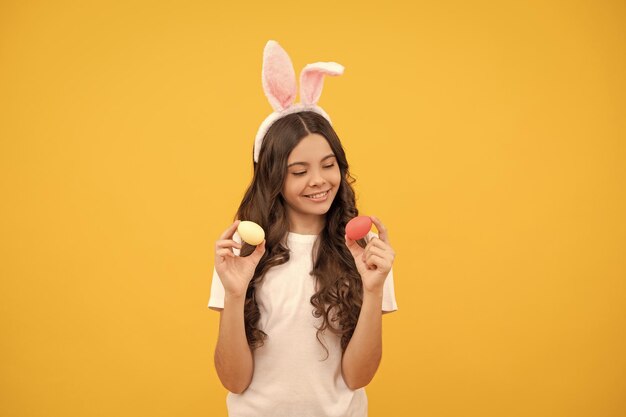 Foto criança positiva em orelhas de coelho segura ovos em fundo amarelo feliz páscoa