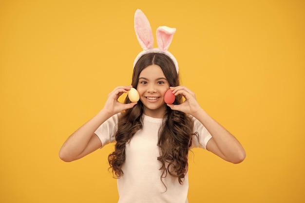 Foto criança positiva em orelhas de coelho segura ovos em fundo amarelo feliz páscoa