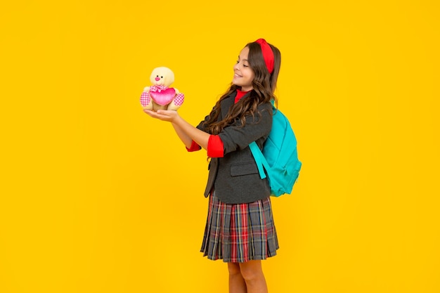 Criança positiva em uniforme escolar e mochila com brinquedo na infância de fundo amarelo