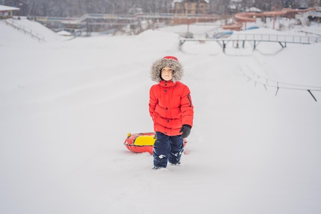 Criança se divertindo em um tubo de neve Menino está montando um tubo de inverno divertido para crianças