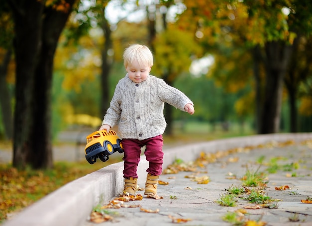 Criança se divertindo no parque outono. Garoto jogando com o carro de brinquedo ao ar livre