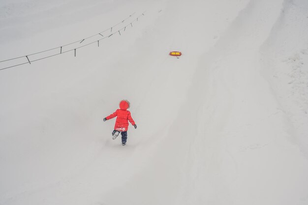 Criança se divertindo no tubo de neve Menino está andando de tubo Diversão de inverno para crianças