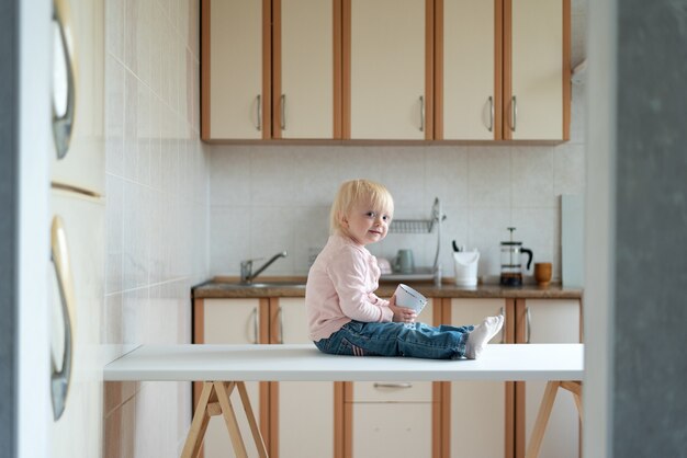 Criança se senta na mesa da cozinha e espera pela mãe. Café da manhã em casa.