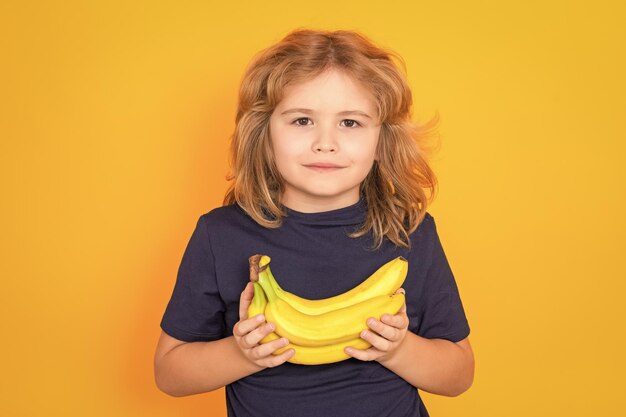 Criança segura banana no estúdio Retrato de estúdio de um menino bonito com bananas isoladas no espaço de cópia de fundo amarelo