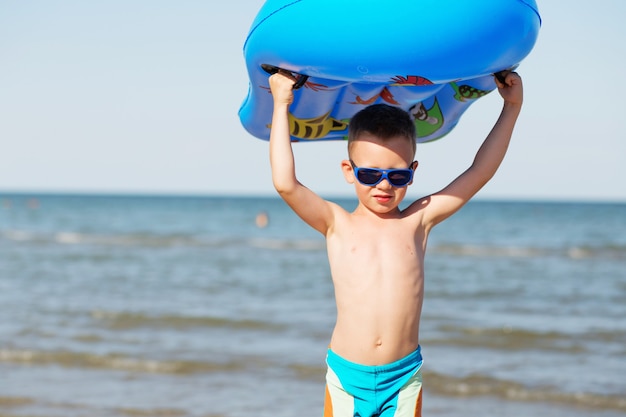 Criança segurando um colchão inflável na praia em um dia quente de verão