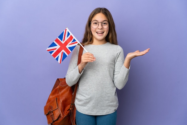 Criança segurando uma bandeira do Reino Unido em uma parede isolada com expressão facial de choque