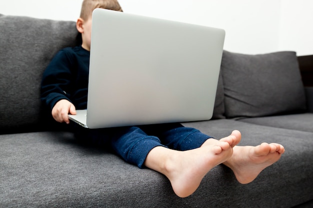 Criança sentada em um sofá e segurando um laptop