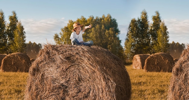 Criança sentada no fardo de feno em um campo