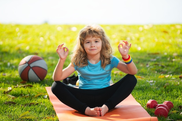 Criança sentada no tapete de rolo praticando ioga meditativa no parque garoto ao ar livre praticando