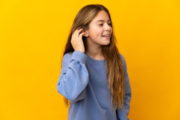 Criança sobre fundo amarelo isolado ouvindo algo colocando a mão na orelha