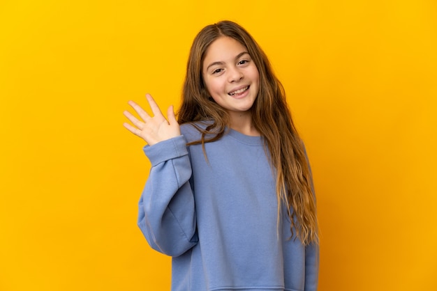 Criança sobre fundo amarelo isolado saudando com a mão com expressão feliz