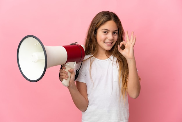 Criança sobre fundo rosa isolado segurando um megafone e mostrando sinal de ok com os dedos