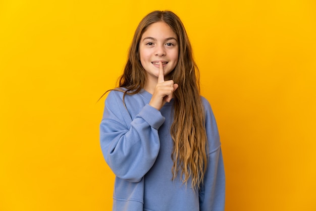 Criança sobre parede amarela isolada mostrando sinal de silêncio gesto de colocar o dedo na boca