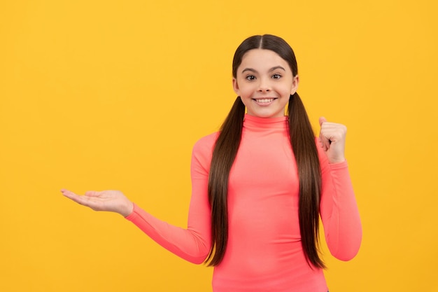 Criança sorridente apresentando espaço de cópia do produto publicidade de menina muito adolescente em fundo amarelo retrato de anúncio de criança feliz venda de compras e oferta de desconto e sugerir proposta de produto