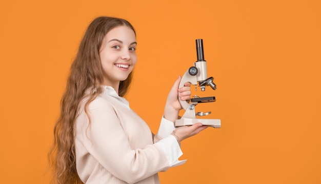 Criança sorridente com microscópio em fundo amarelo