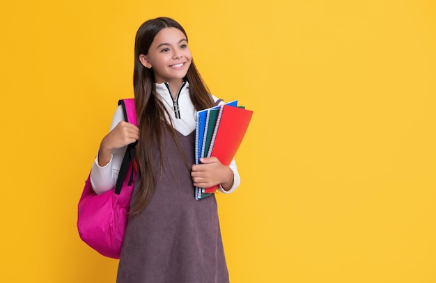 Criança sorridente com mochila escolar e livro de exercícios em fundo amarelo