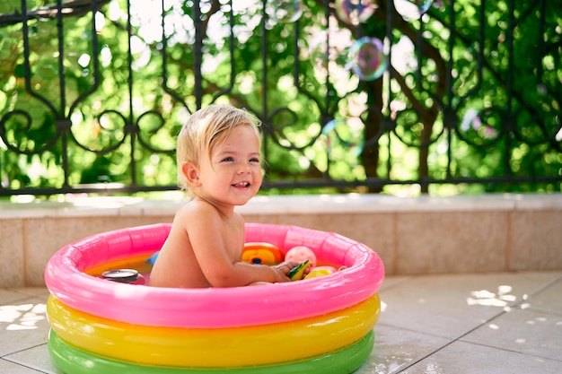 Criança sorridente e molhada sentada em uma pequena piscina inflável com brinquedos