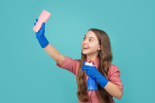 Criança sorridente em luvas de borracha com frasco de spray e pano de microfibra sobre fundo azul