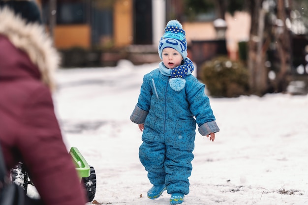 Criança sorridente em roupas de inverno com chapéu e lenço, desfrutando na neve.