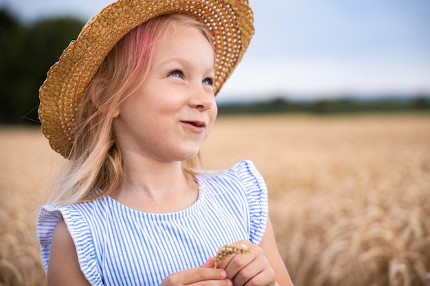 Foto criança sorridente, menina loira, usando um chapéu em um campo de trigo