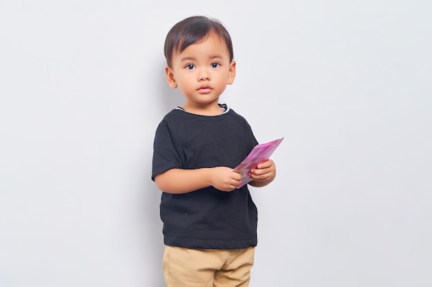 Criança sorridente menino de 2 anos vestindo camiseta preta segurando notas de rupia indonésias isoladas em fundo branco