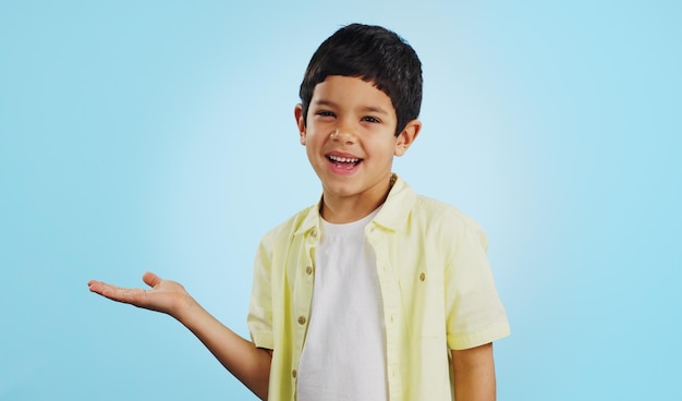 Foto criança sorrindo e feliz para a apresentação no estúdio em fundo azul com modelo para colocação de produtos menino jovem e animado para oferta de oportunidade ou negócio em mídia social de aplicativo ou marketing digital