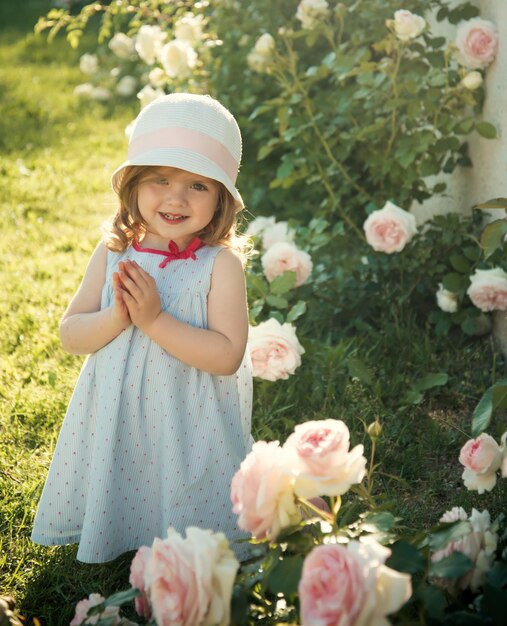 Criança sorrindo para flores rosas desabrochando na grama verde