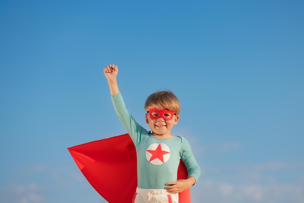 Criança super-herói brincando ao ar livre. Garoto super-herói contra o fundo do céu azul de verão. Conceito de imaginação e liberdade