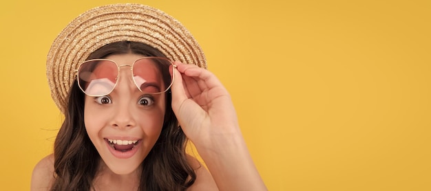 Criança surpreendida com chapéu de palha de verão e óculos tem cabelos cacheados em fundo amarelo moda de praia Cartaz horizontal de rosto de criança adolescente menina isolado banner de retrato com espaço de cópia