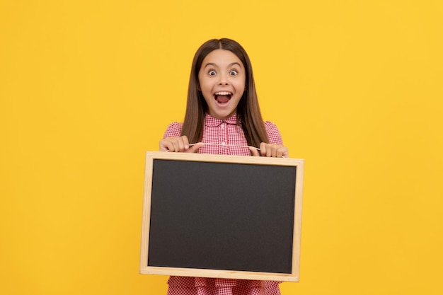 Criança surpreendida segura quadro-negro escolar para anúncio de espaço de cópia